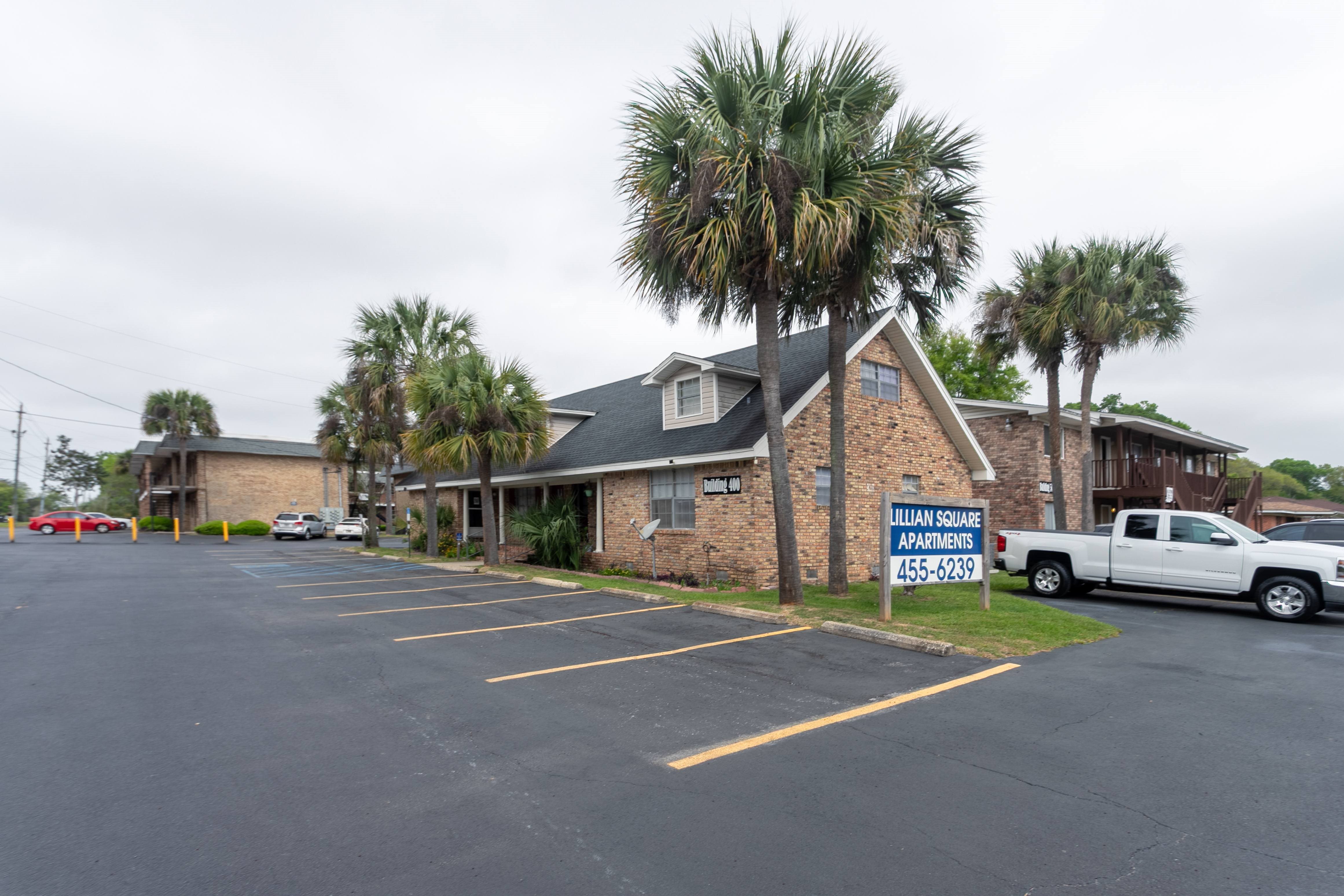 A parking lot in front of a brick building with a sign that says "William Square Apartments" and a phone number.
